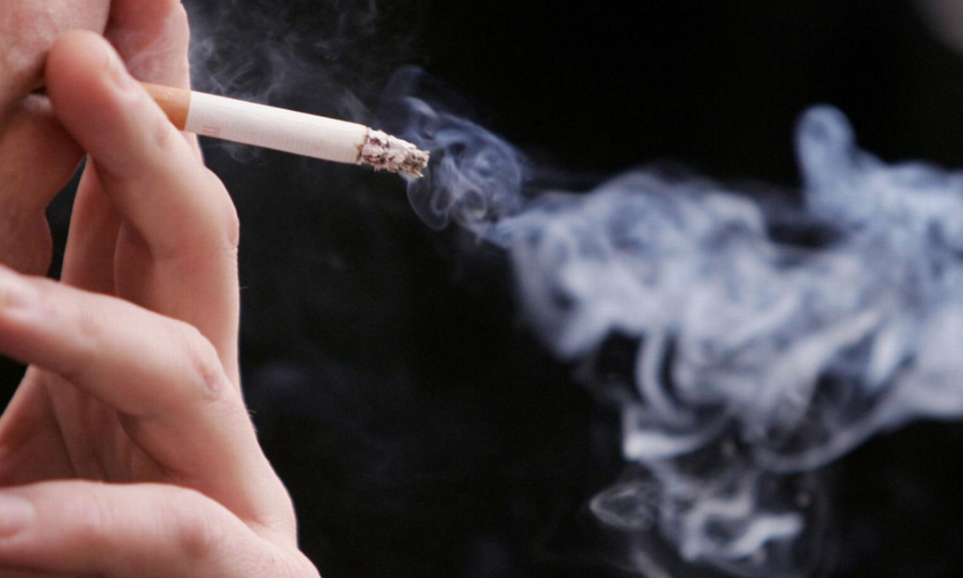 Cigarro aceso entre os dedos com fumaça